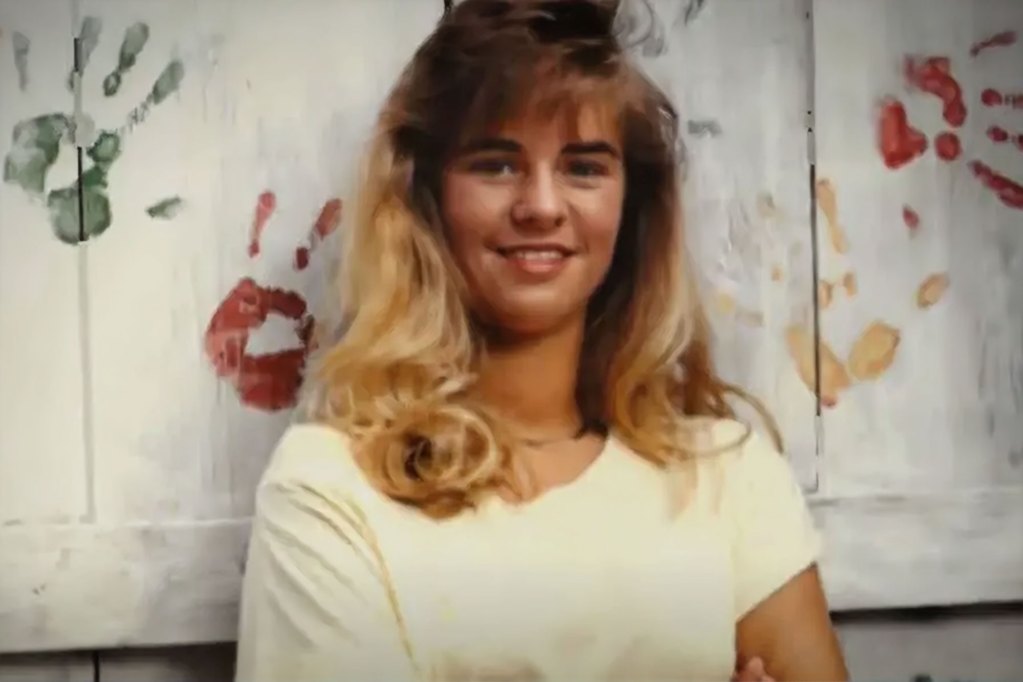 An old photo of Kristy Ray taken in front of a white fence with colorful handprints painted on it
