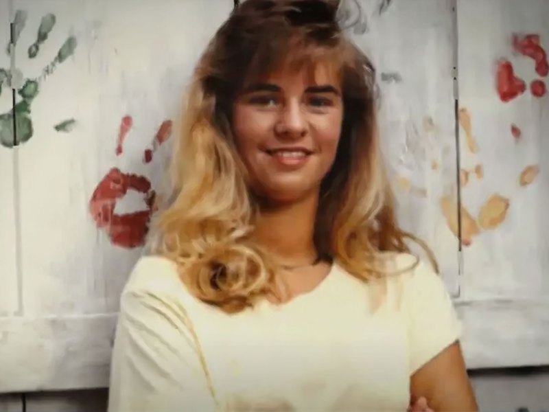 An old photo of Kristie Ray taken in front of a white fence with colorful handprints painted on it