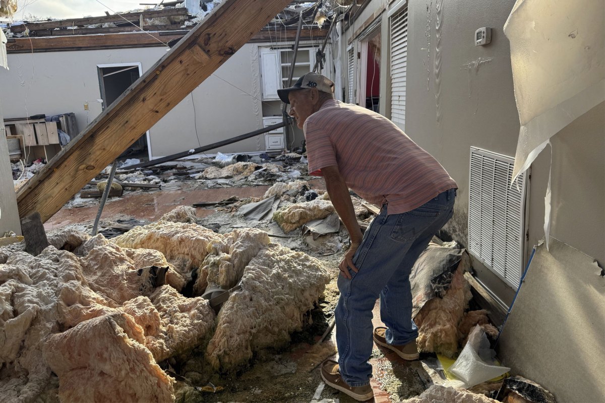 A man in a striped shirt and jeans surveys what's left of a tornado destroyed home