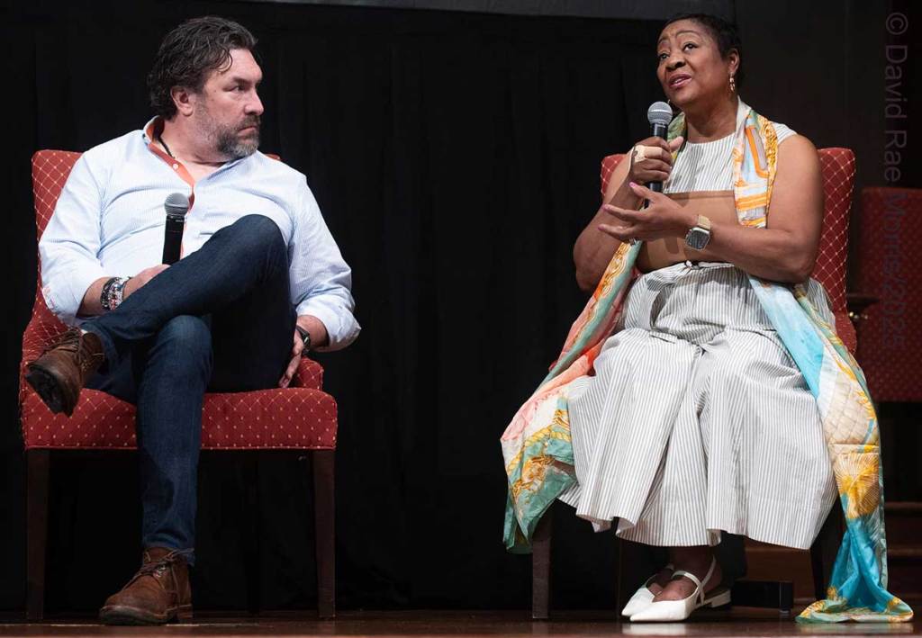 Two people seated on a stage seen talking for a panel
