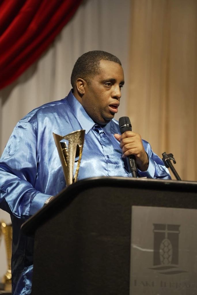 Man standing at podium speaking into microphone and holding a trophy