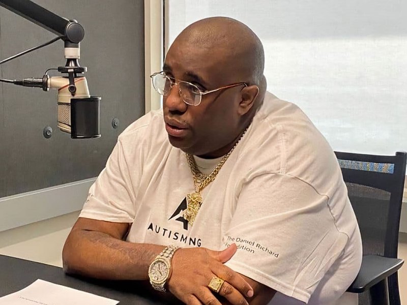 A man wearing glasses, sitting at a desk behind a podcast speaker