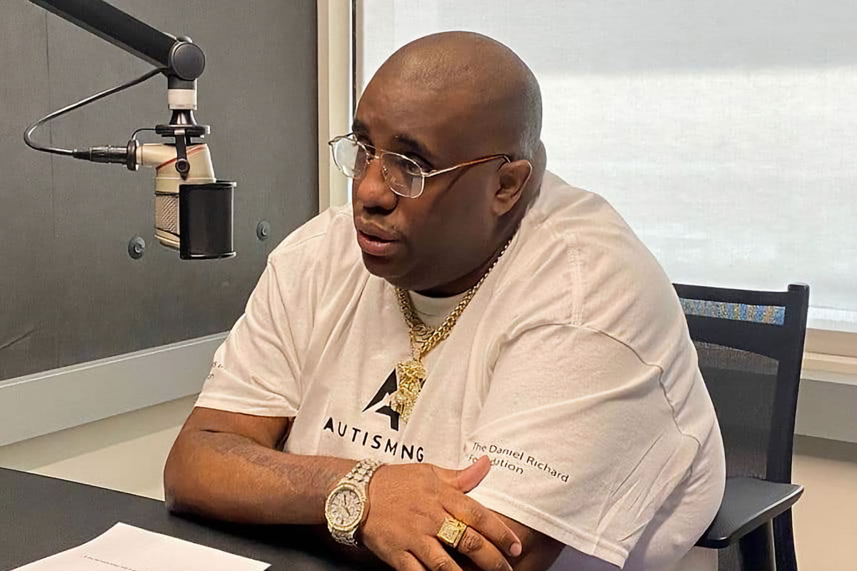 A man wearing glasses, sitting at a desk behind a podcast speaker