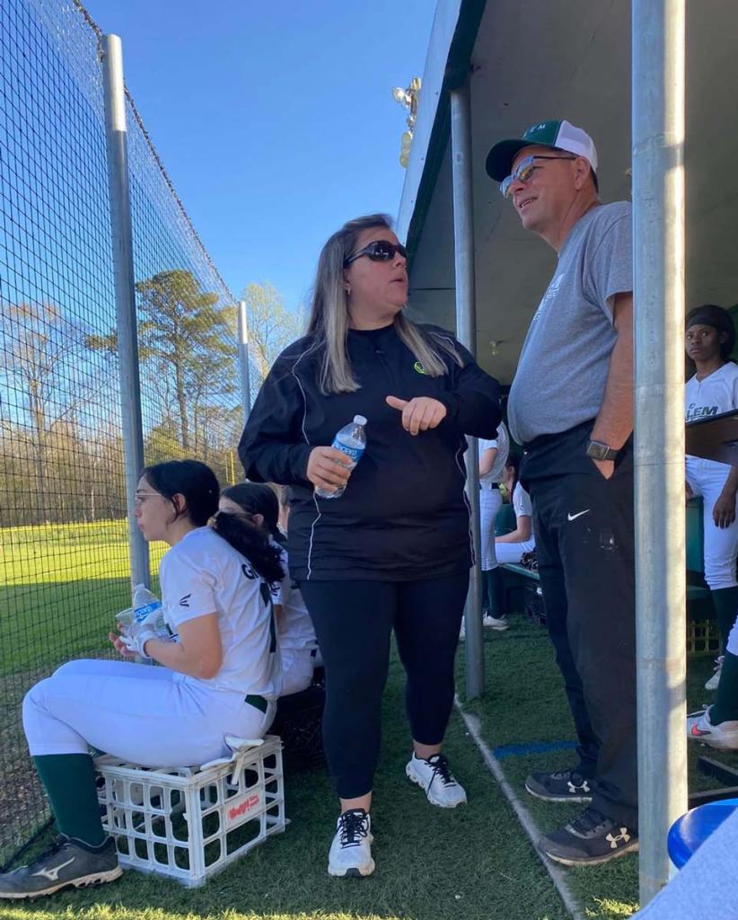 A man and woman stand in the dugout of a softball team