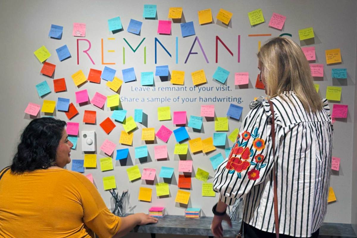 Two women add colorful sticky notes to a wall that reads REMNANTS in rainbow colors
