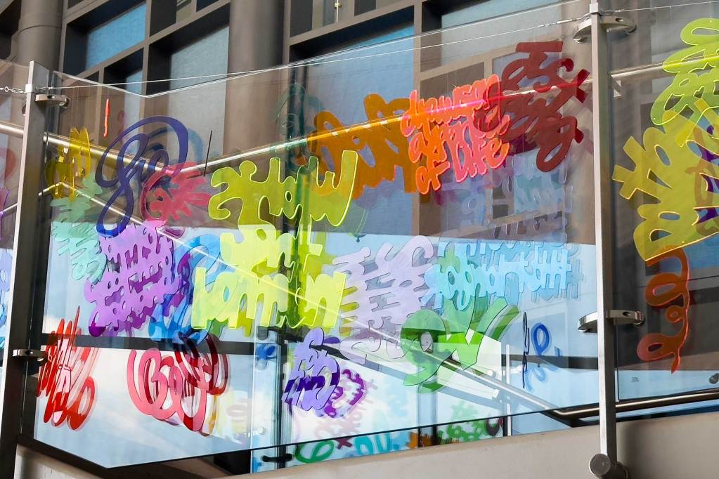 Colorful acrylic text hangs from a glass stairwell wall