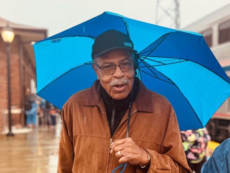 A man stands in the rain under a blue umbrella