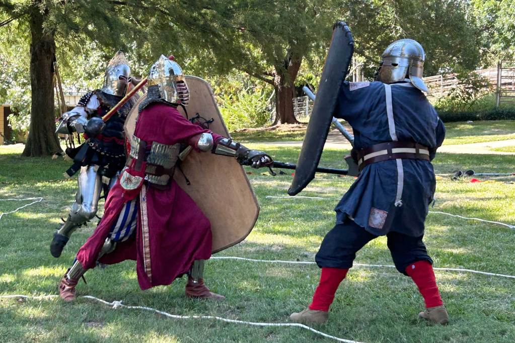 People in armor, shields and swords practice fighting outside