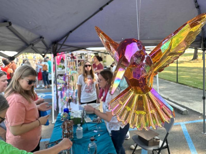 A crystal hummingbird hangs at a market attended by many people