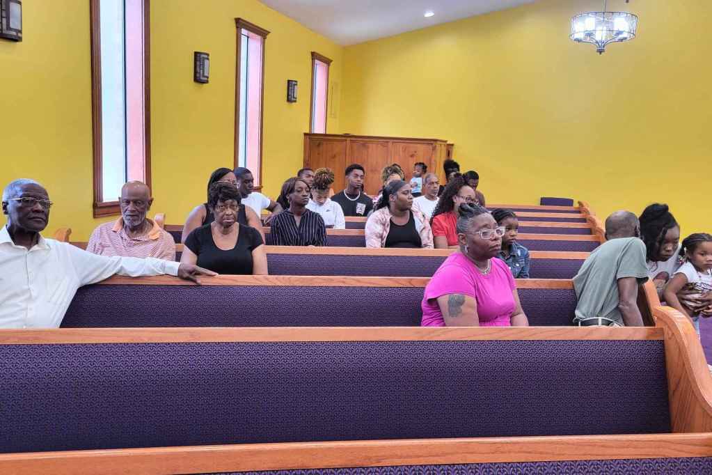Family and community members sit in the pews of a church with yellow walls