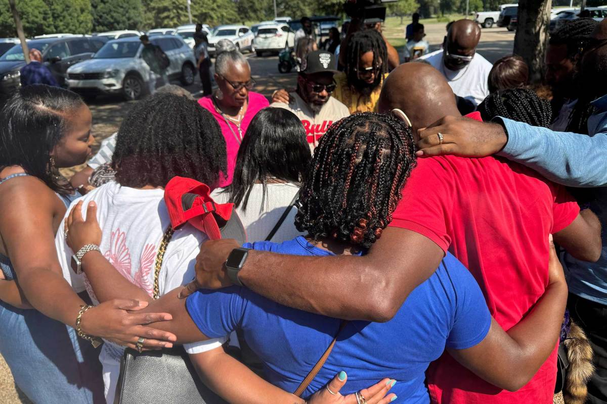 People gather in a prayer circle, arms entwined, outside near a parkinglot