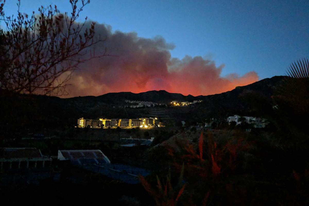 Smoke glowing red from the fire below as seen from the other side of a hill