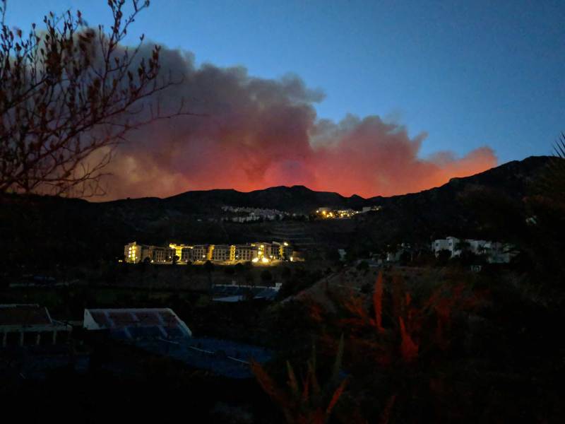 Smoke glowing red from the fire below as seen from the other side of a hill