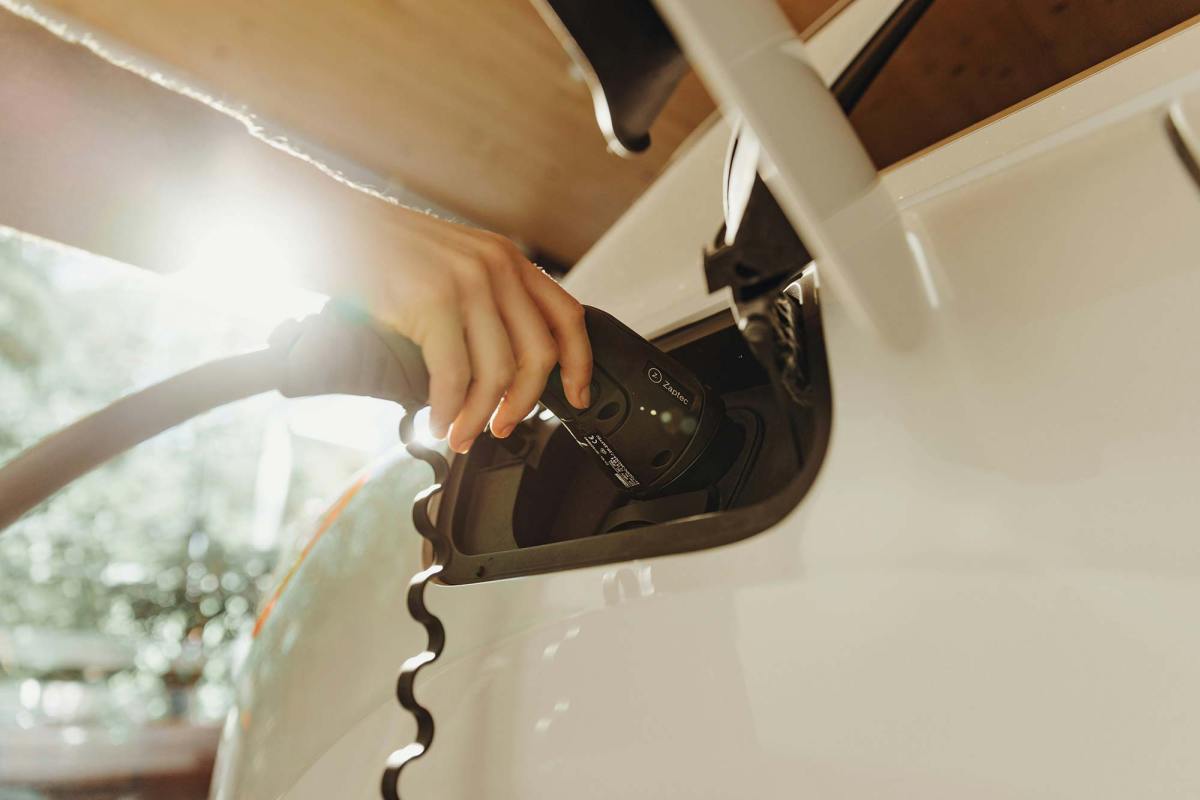 A hand is seen charging a white electric car