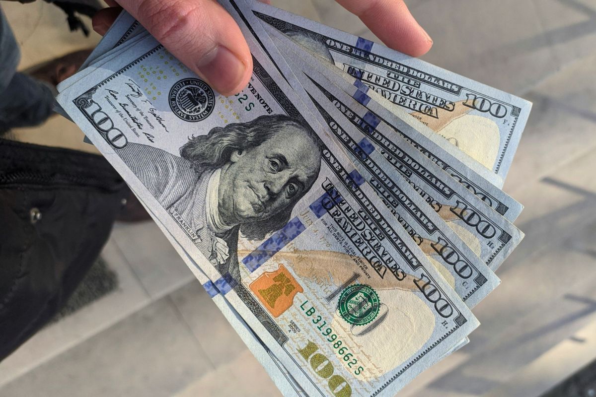 A hand holding 6 one hundred dollar bills