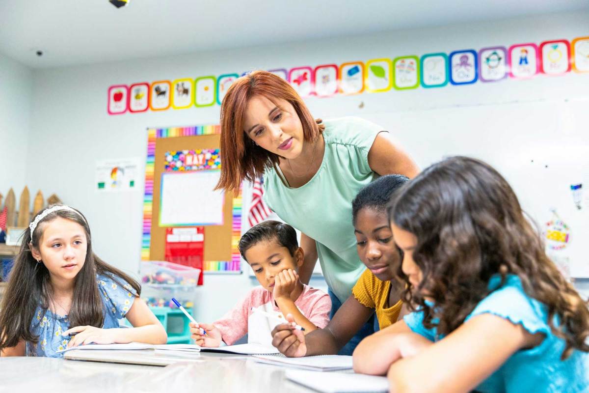 A young female teacher monitors students working on a writing lesson