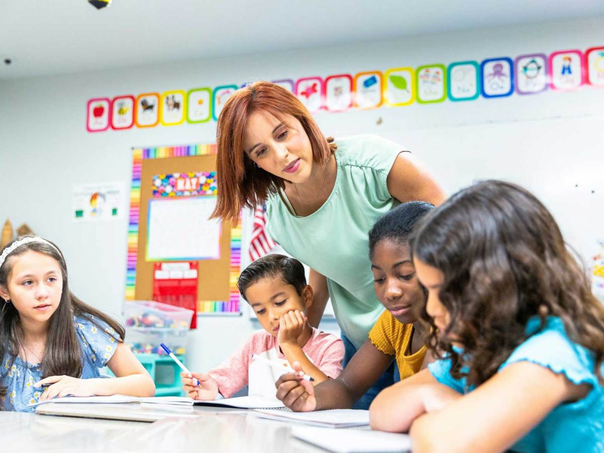 A young female teacher monitors students working on a writing lesson