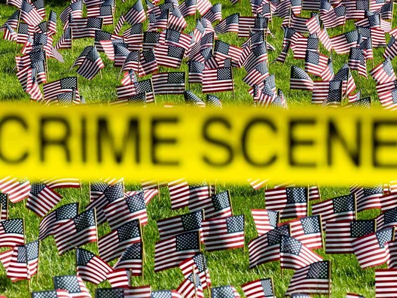 A lawn covered in small US Flags is blocked by a yellow CRIME SCENE banner