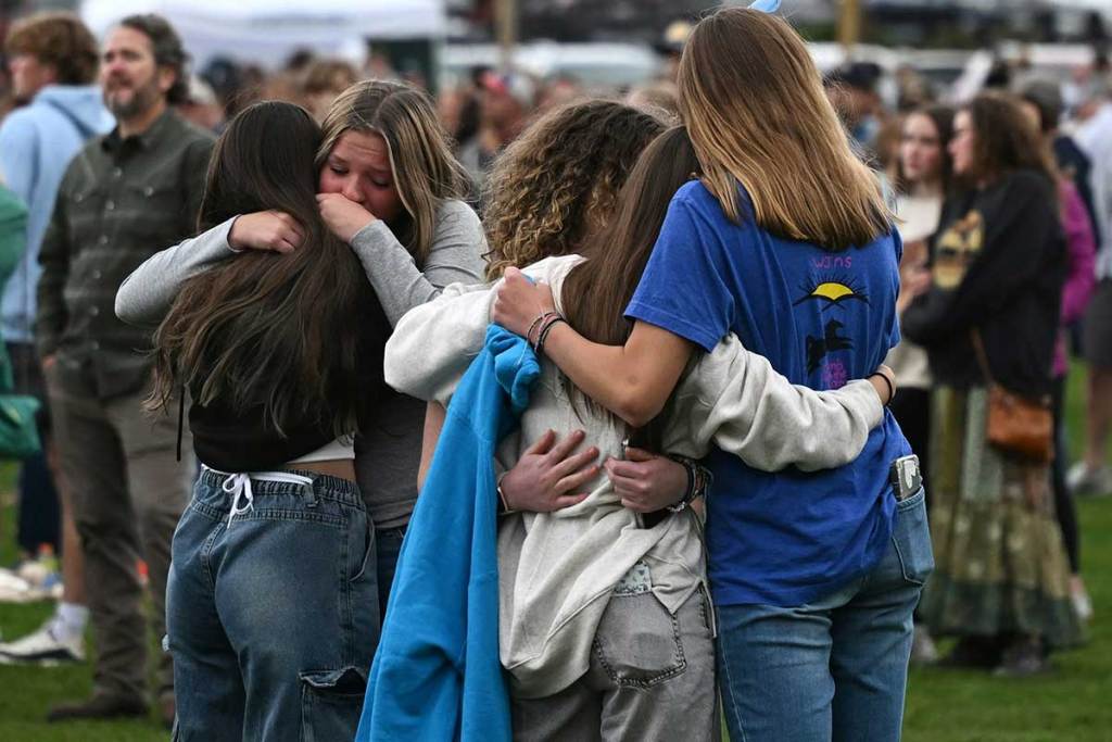 High school age children embrace in the foreground, with other bystanders in the background