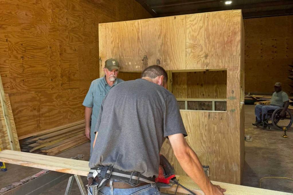 Two men cutting wooden planks on a sawhorse
