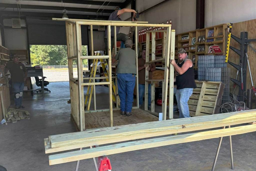 Three men assembling a wooden structure inside a large workshop