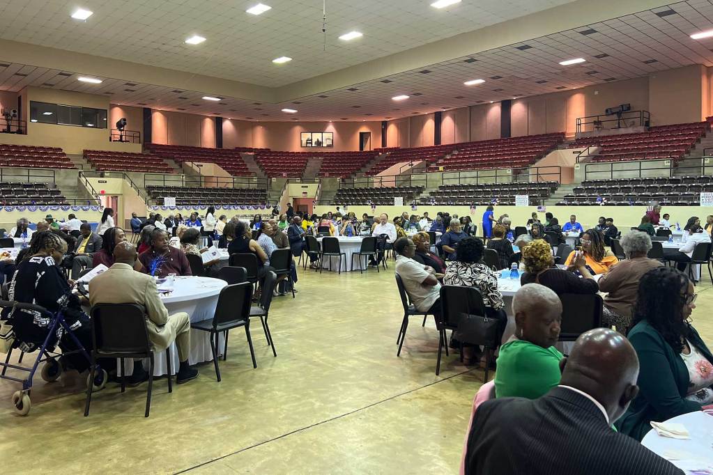 An auditorium is filled with people sitting at round banquet tables
