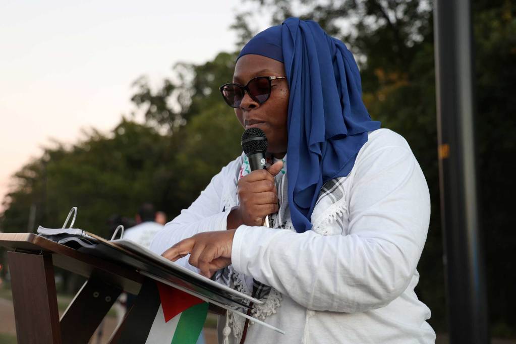 A woman in a blue head wrap speaks at a vigil
