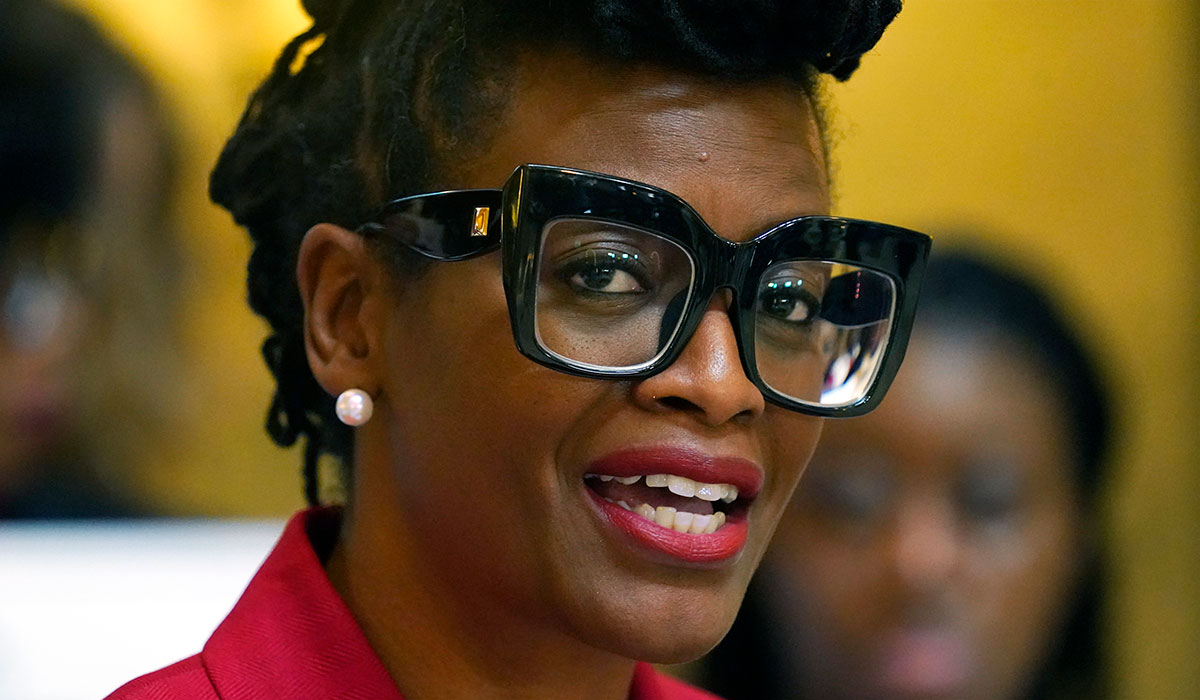 A closeup of a woman in a red top and black glasses speaking