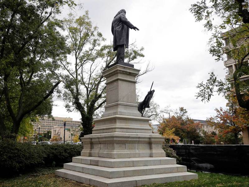 A confederate statue of a man on a tall pedestal located in a park