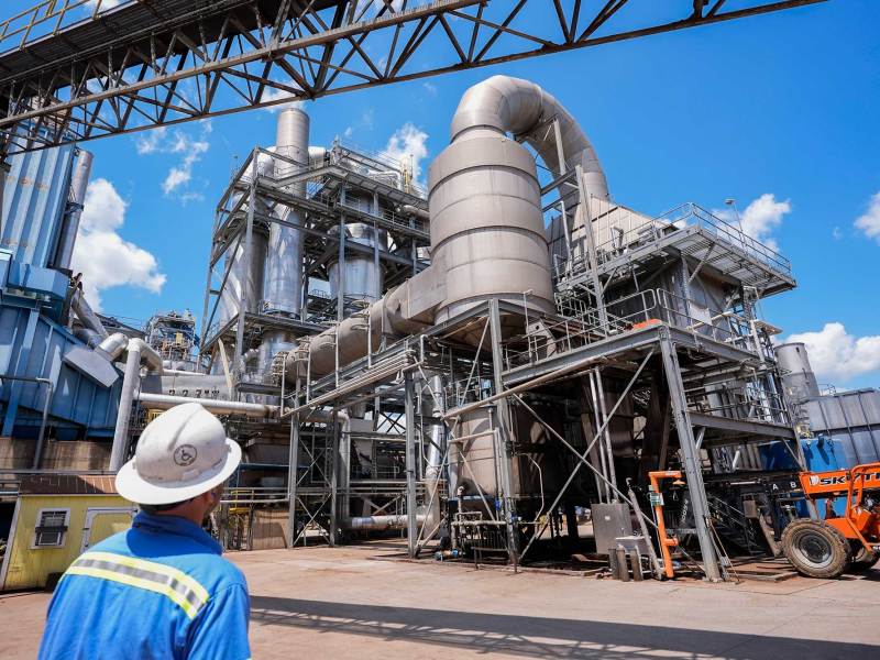 A man in a hardhat looks on at a large industrial facility outside