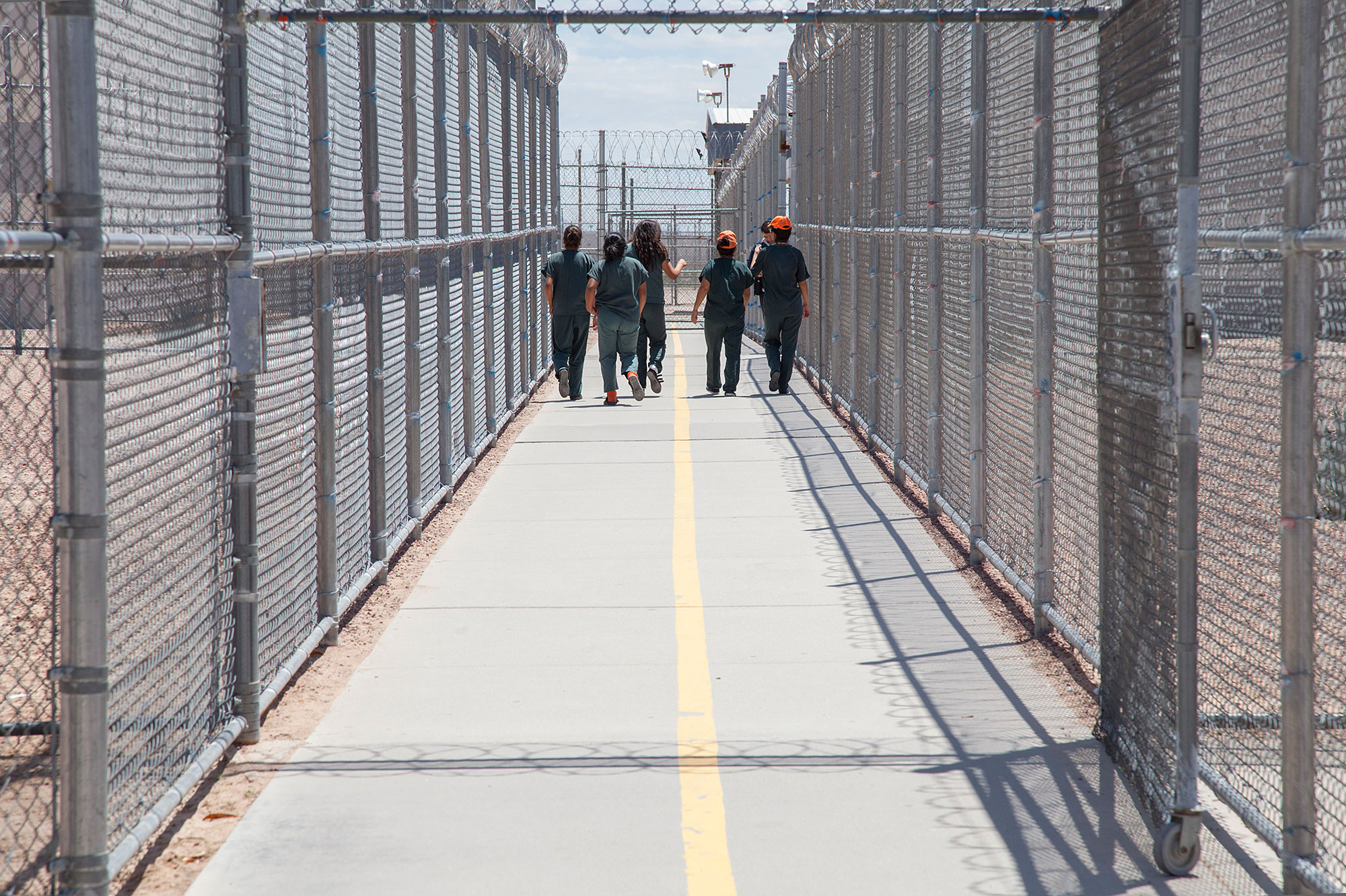 People in matching jumpers walking down a fenced path in a detention facility
