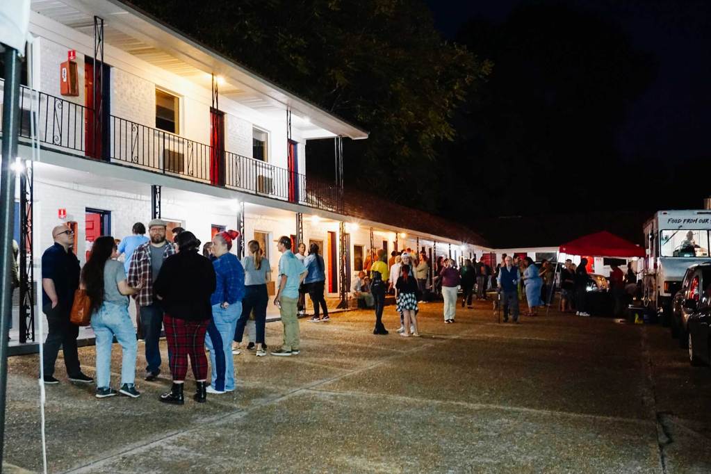 A crowd of people attend an art show at a motel at night