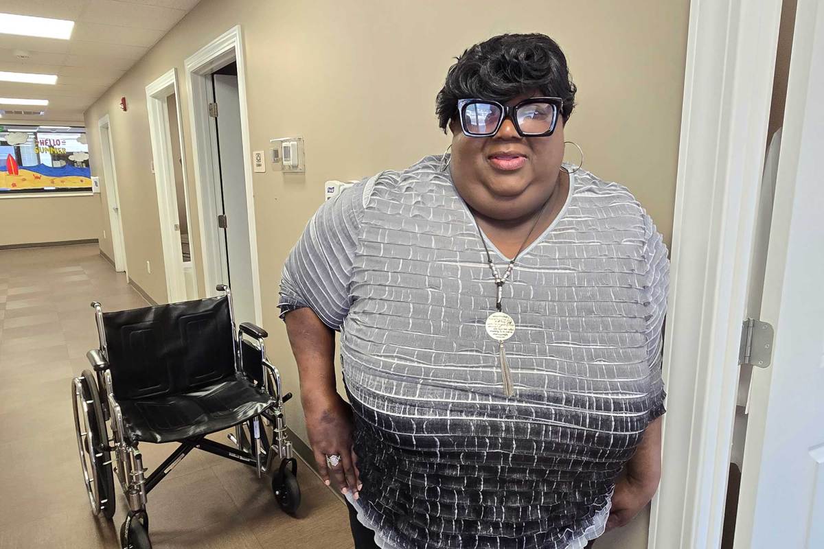 A Black woman standing next to a door frame with a wheelchair in the background