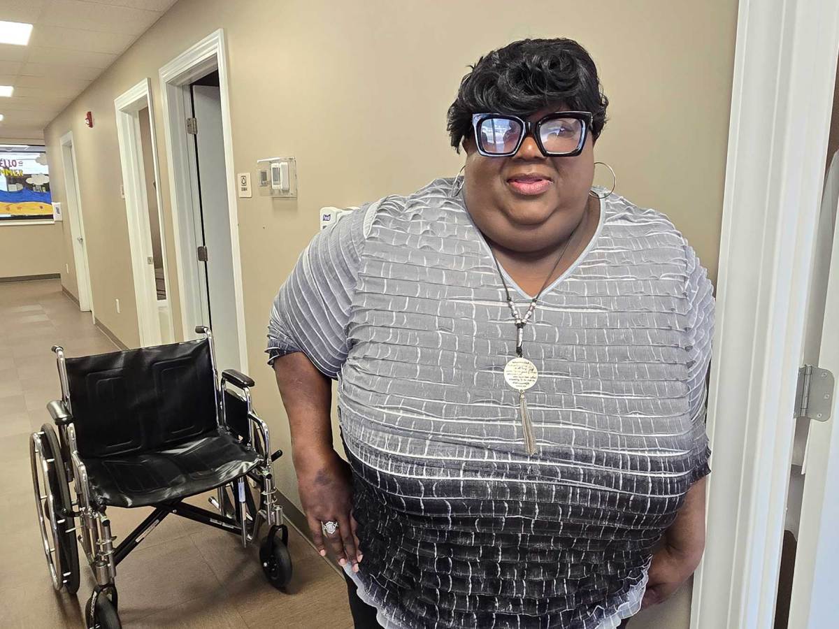 A Black woman standing next to a door frame with a wheelchair in the background