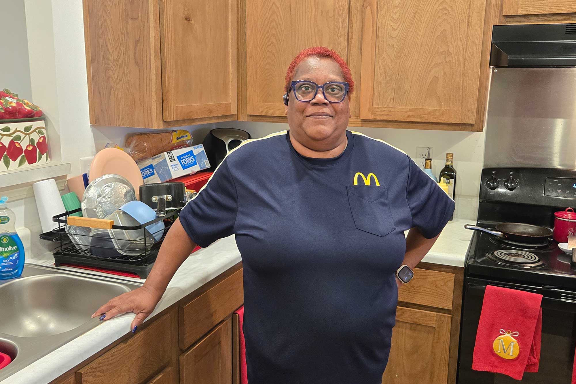 A Black woman standing in a kitchen with her right hand resting against the sink frame