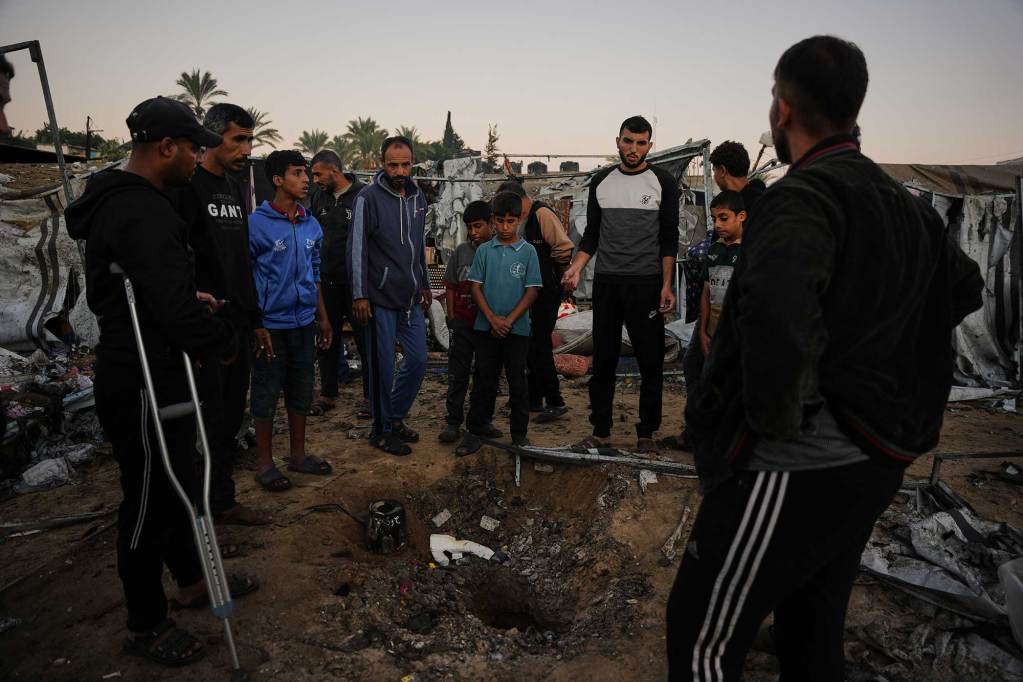 A group of Palestinians gathered in a circle with damaged buildings and ruins surrounding them.