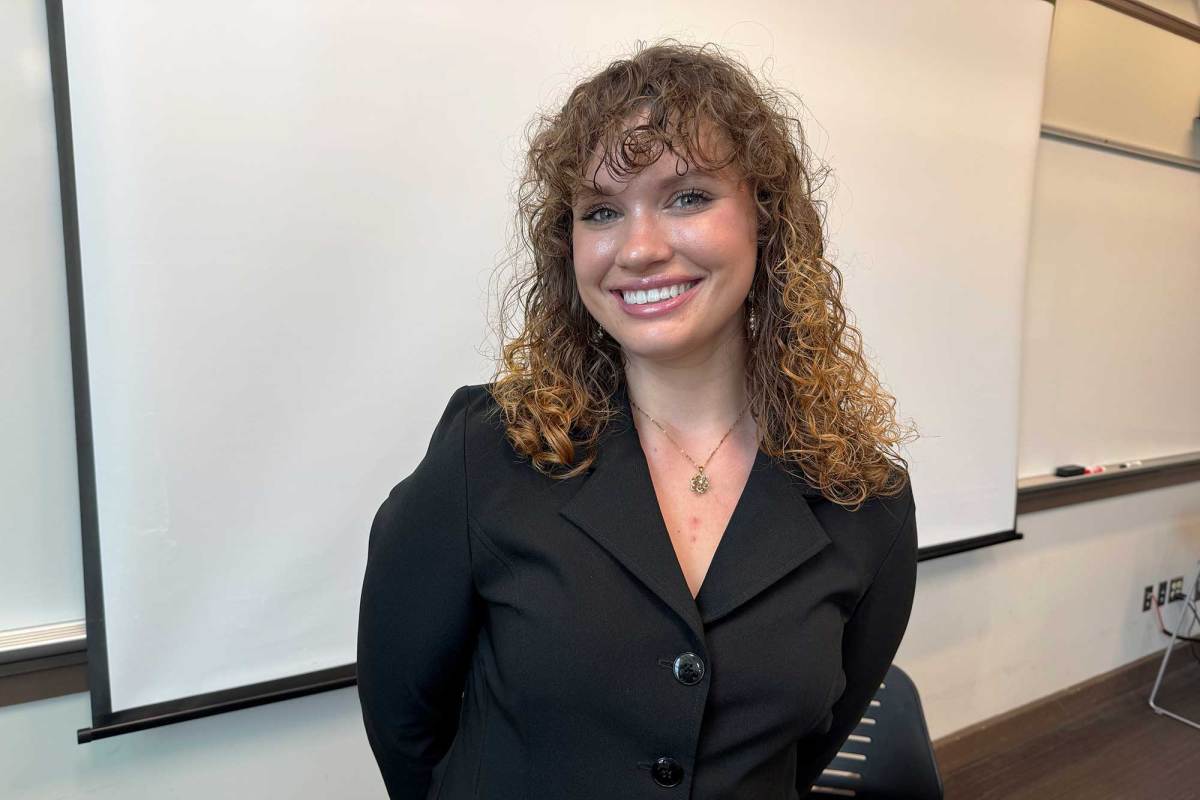 A woman with curly brown hair and wearing a black shirt smiling in front of a classroom whiteboard