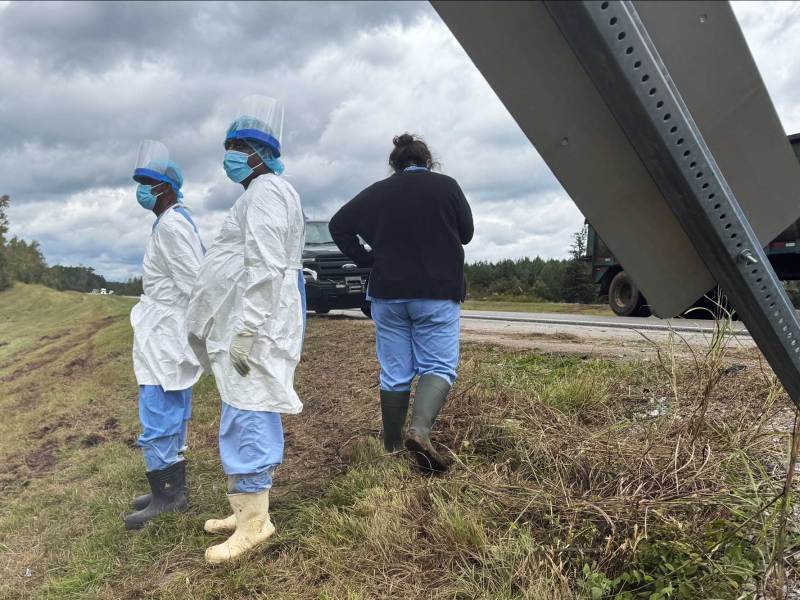 Three people on the side of a highway wearing personal protective equipment including scrubs, face masks and gloves.