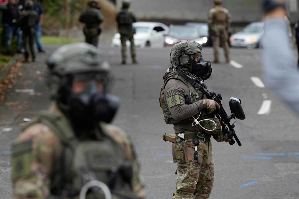 ICE Agent in gas masks and carrying guns stand in a road
