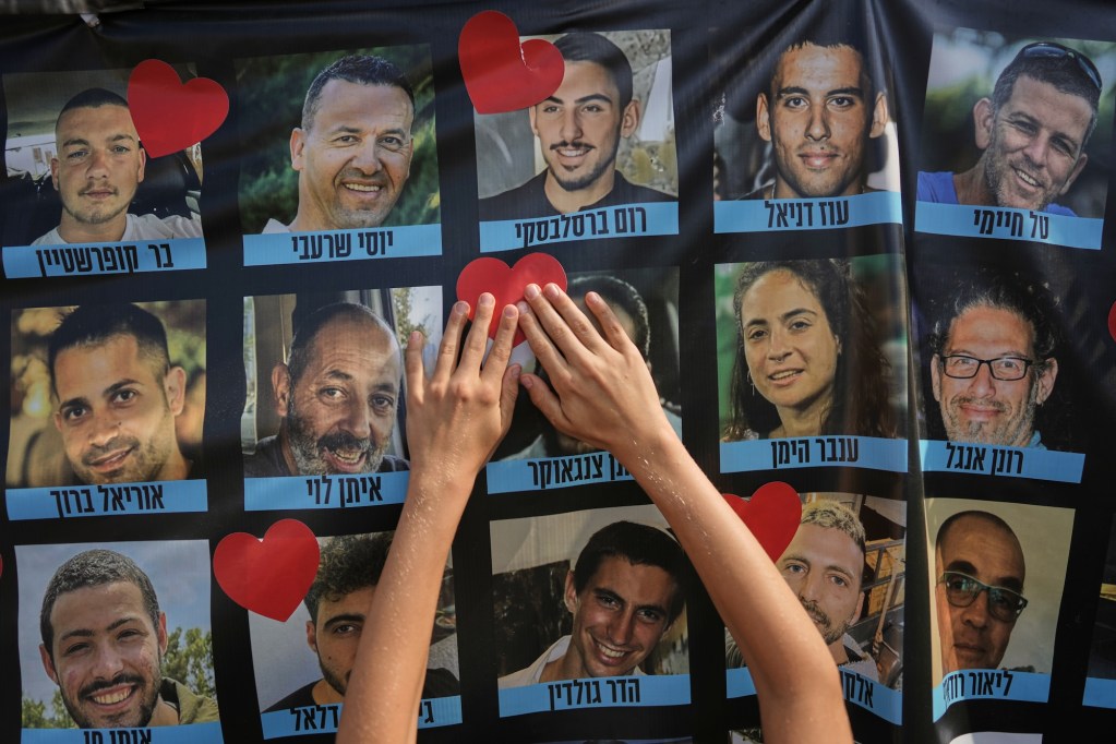 two small hands put a heart sticker on a man's face in a collage of men and women who are Israeli hostages with names written in Hebrew