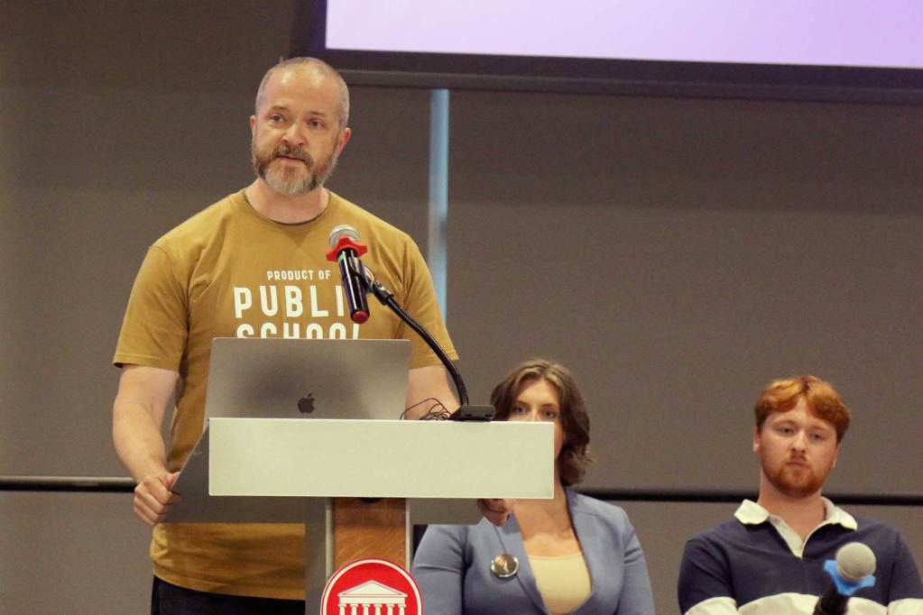 James Thomas, wearing a shirt that reads 'Product of Public School' speaks at a town hall