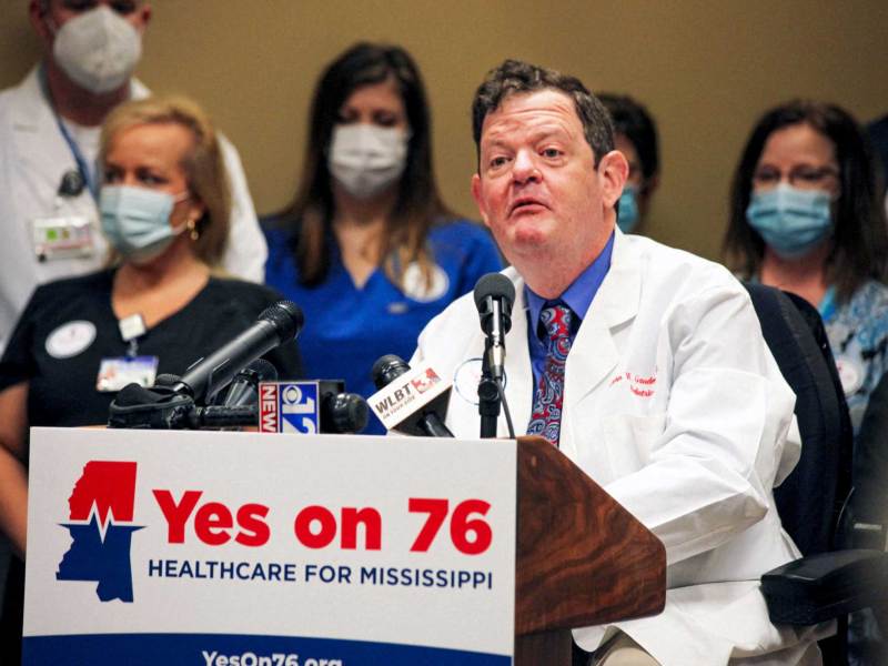 Dr. John Gaudet speaking behind a podium. A sign on the podium reads, “Yes on 76 Healthcare for Mississippi.”