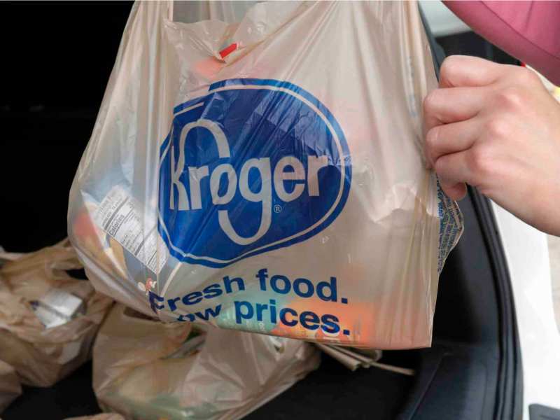 A pair of hands puts a bag of groceries from Kroger into the back of a car