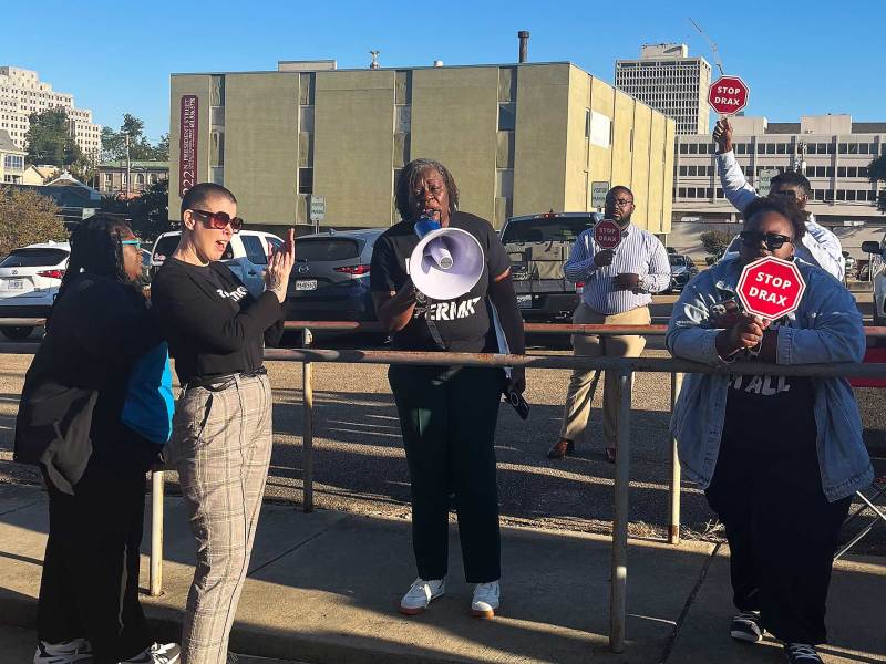 A woman flaps as she listens to someone else speak on a megaphone at a small "Stop Drax' rally
