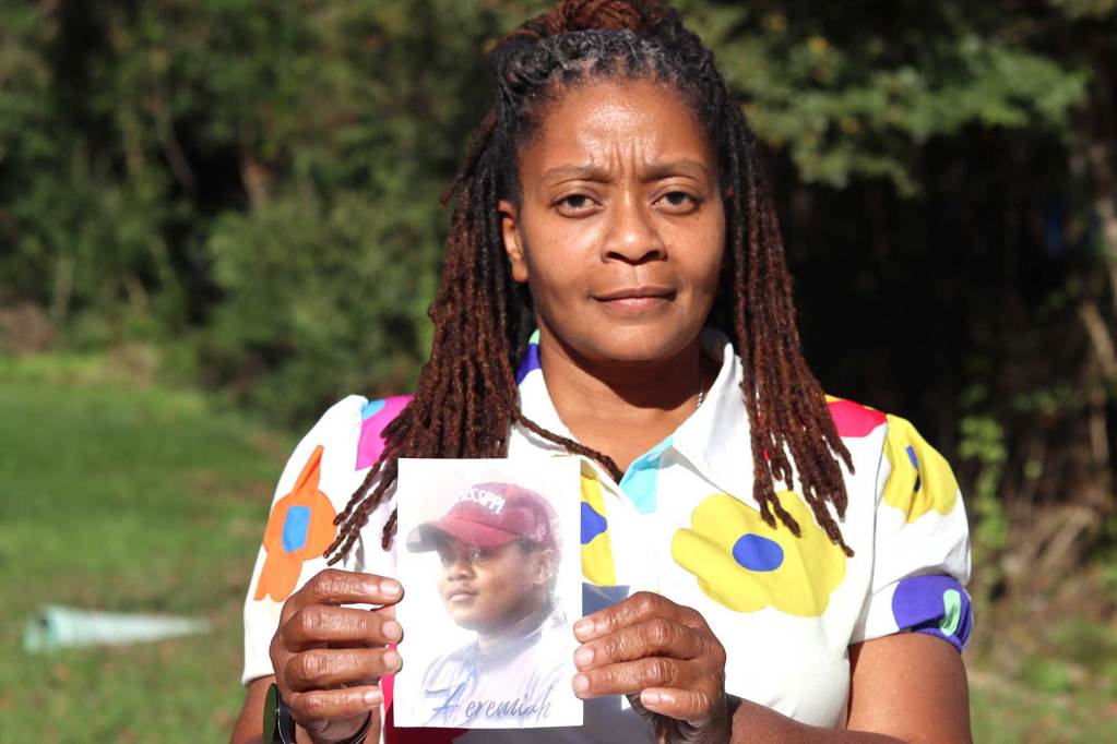 A woman in a floral print top holds up a photo of a boy in a red baseball cap