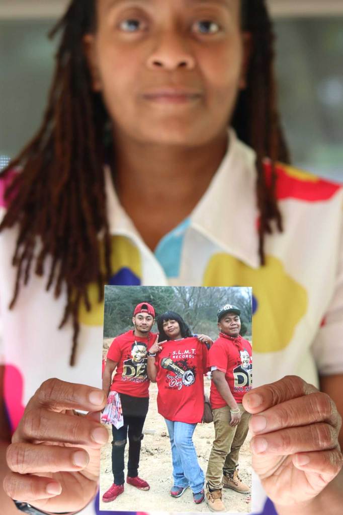 A woman in a floral shirt holds up a photo of three people in matching red shirts