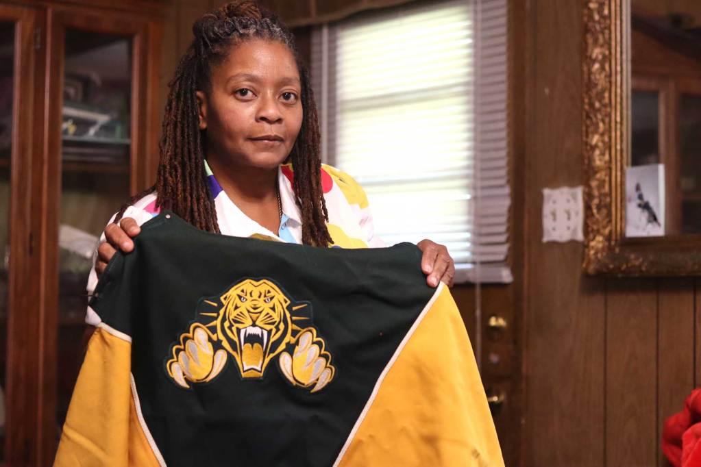 A woman holds up a black and gold jacket with a tiger on the back