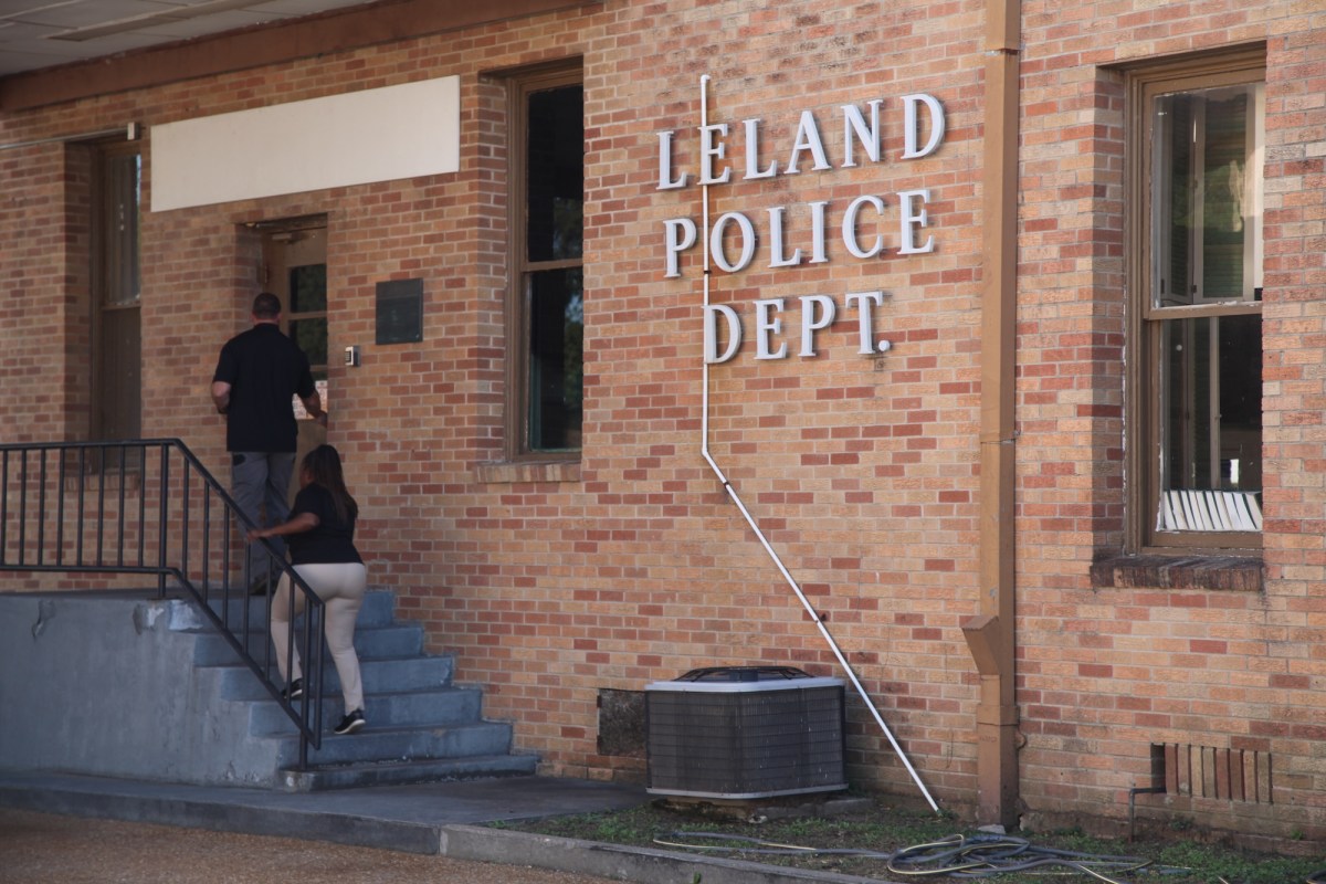 the side of a brick building is seen with two people walking up a set of steps to a door. The words "Leland Police Dept." are on the side of the building