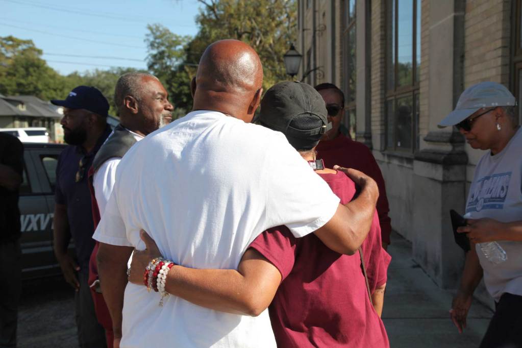 A man wearing a white shirt and a woman wearing a maroon shirt embrace with their backs to the camera.