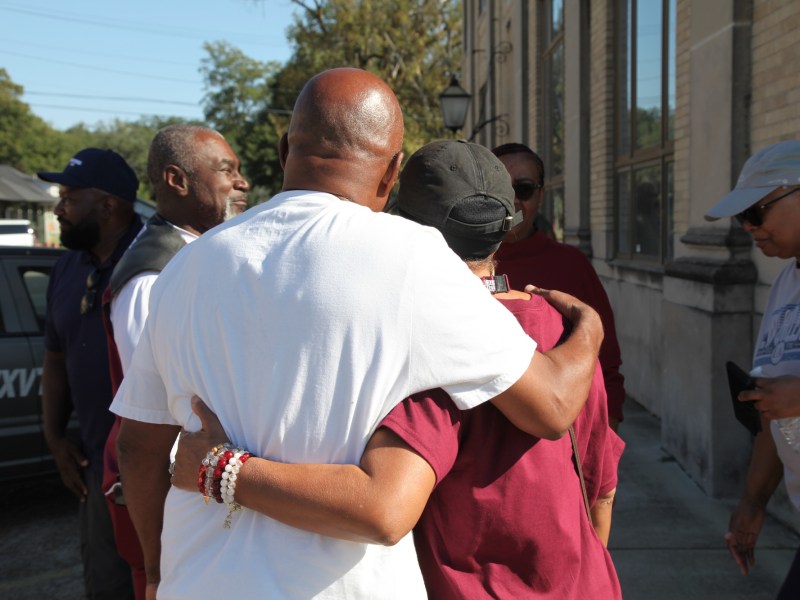 A man wearing a white shirt and a woman wearing a maroon shirt embrace with their backs to the camera.